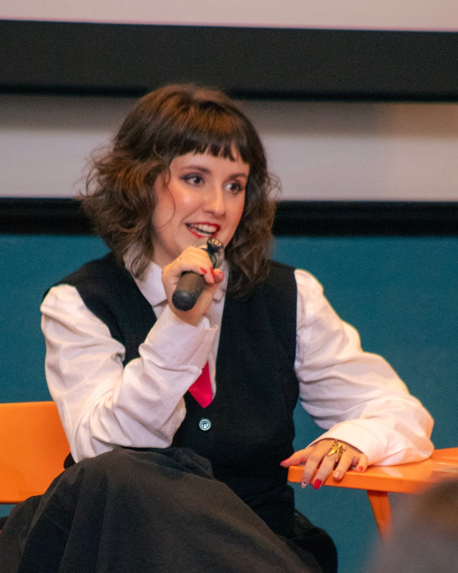 Paloma Pena Firme sentada a uma mesa, de microfone na mão, conduzindo uma conversa para uma roda de pessoas.
